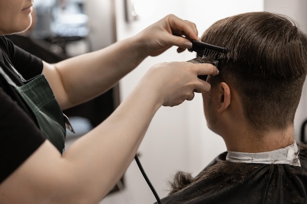 Ein Mann schneidet sich in einem Friseursalon mit einer Haarschneidemaschine die Haare an den Schläfen