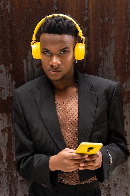 Ein Mann schwarzer Ethnizität, der Musik hört, kabellose gelbe Kopfhörer, die Musik auf digitalen Plattformen mit dem Telefon hören