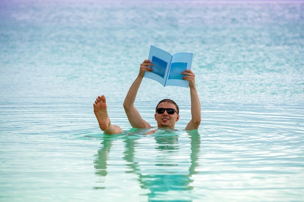 Ein Mann schwimmt mit einer Zeitschrift in der Hand auf dem Rücken im Toten Meer