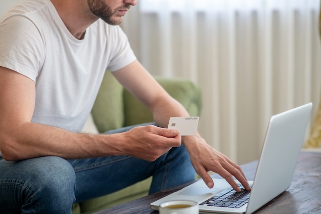 Ein Mann sitzt am Laptop und zahlt online mit Kreditkarte