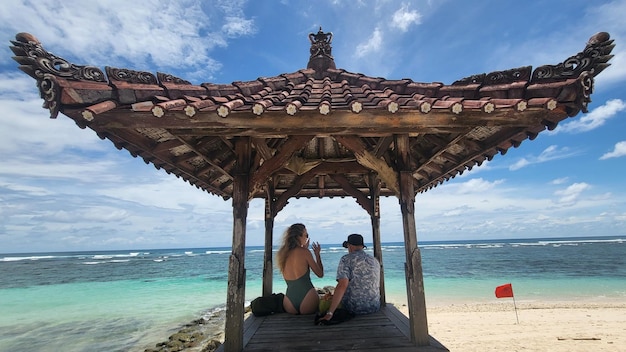Ein Mann sitzt an einem Strand vor einem Pavillon mit einer Frau, die einen Bikini am Strand von Pandawa in Indonesien trägt