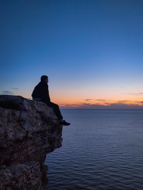 Ein Mann sitzt auf einem Felsen am Meer