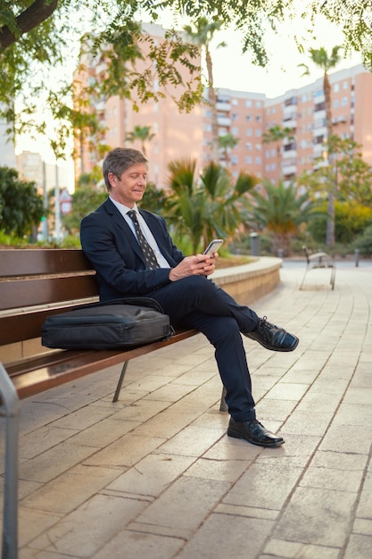 Foto ein mann sitzt auf einer bank und schreibt auf einem handy