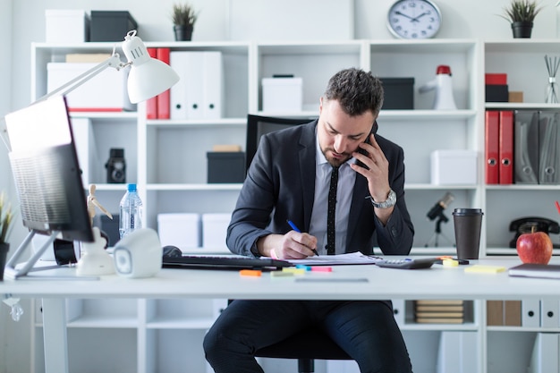 Ein Mann sitzt im Büro am Tisch, telefoniert und arbeitet mit Dokumenten.