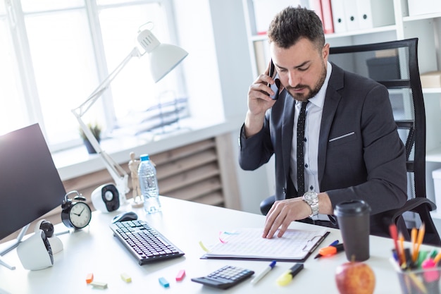 Ein Mann sitzt im Büro am Tisch, telefoniert und blättert durch Dokumente.