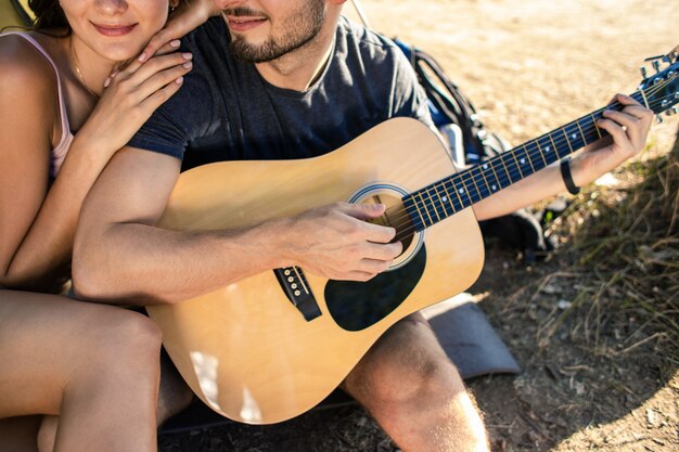 Ein Mann spielt für eine Frau auf einer Gitarre in der Nähe eines Zeltes bei Sonnenuntergang. Flitterwochen in der Wanderung
