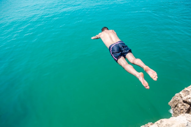 Ein Mann springt von einer Klippe ins Wasser.