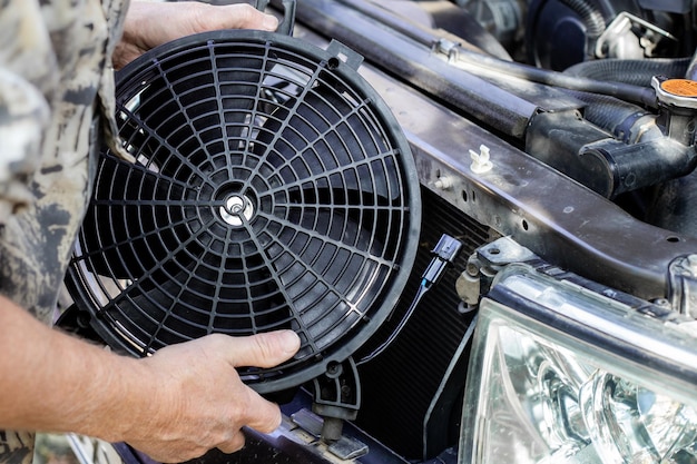 Foto ein mann steckt einen motorkühlventilator unter den kühlergrill eines autos ein maschinenwartung und -reparatur