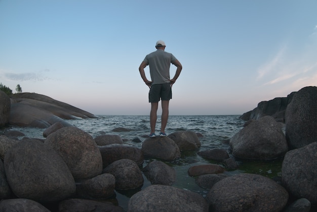 Ein Mann steht am Ufer einer felsigen Lagune. Rückansicht