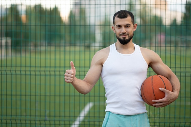 Ein Mann steht am Zaun auf der Straße, hält einen Basketball in der Hand und zeigt sich cool