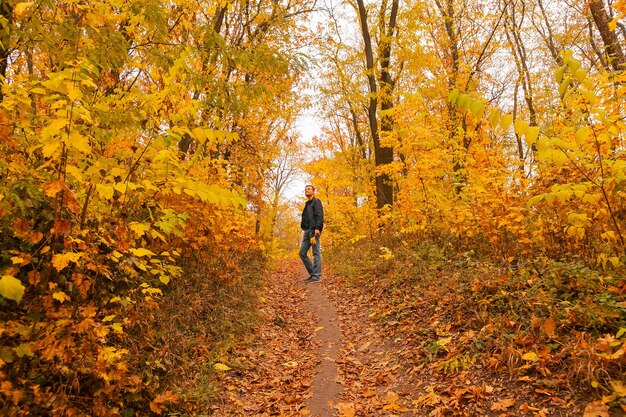 Ein Mann steht auf dem Weg durch den herbstlichen Wald, zwischen Bäumen und Sträuchern, ein Ahornblatt in den Händen, genießt Herbst und Natur