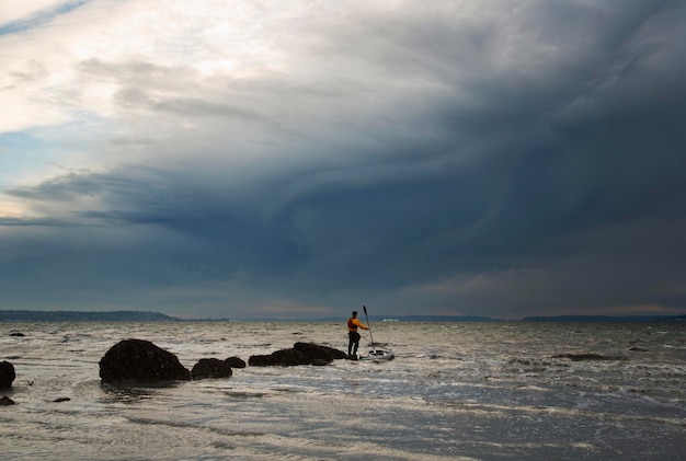Ein Mann steht auf einem Felsen mitten im Puget Sound, sein Seekajak schwimmt neben ihm