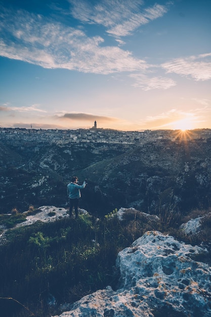 Ein Mann steht bei Sonnenuntergang auf einem Felsen im Stadtbild