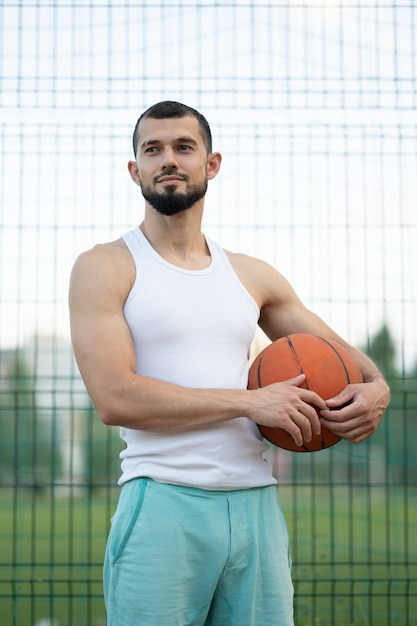 Foto ein mann steht in der nähe eines zauns auf der straße und hält einen basketball in der hand