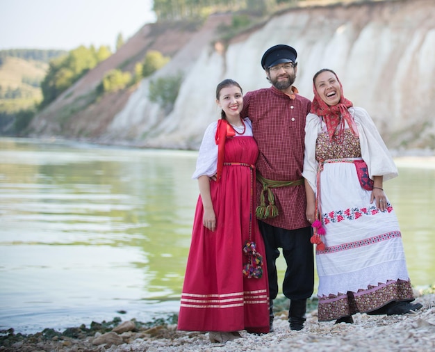 Ein Mann steht in einer Umarmung mit schönen Frauen vor einer wunderschönen Landschaft, alle gekleidet in Nationaltracht, Nahaufnahme