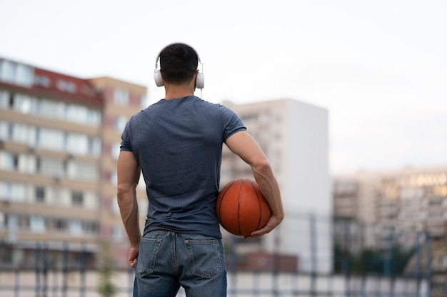 Foto ein mann steht mit dem rücken zur stadt und hält einen basketball in den händen