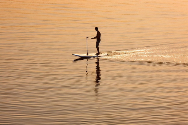 ein Mann steht mit einem Paddel auf einem Surfbrett im Wasser