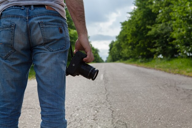 Ein Mann steht mit einer Kamera auf der Straße in der Nähe des Waldes