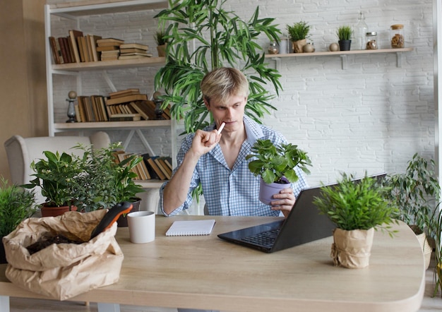 Ein Mann studiert und macht sich Notizen mit einem Laptop, der Zimmerpflanzen studiert, und führt wissenschaftliche Arbeiten zur Erforschung der Botanik durch