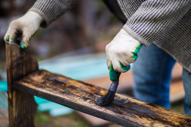 Ein Mann trägt mit einem Pinsel Farbe auf eine Holzoberfläche auf Lackarbeiten
