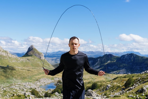 Ein Mann trainiert draußen Porträt eines Athleten, der auf einem Seil vor dem Hintergrund von Berggipfeln springt