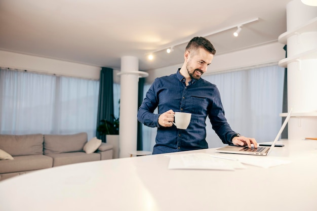 Ein Mann trinkt Kaffee und benutzt einen Laptop zum Online-Surfen in seinem gemütlichen Zuhause