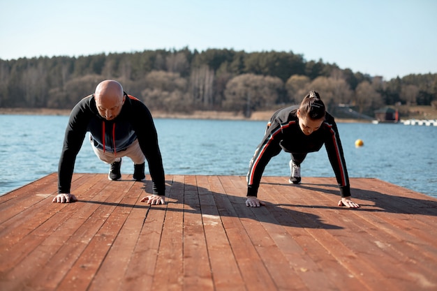 Ein Mann und ein Mädchen in Sportkleidung machen auf dem Pier am See Plankenübungen. Sport, Gesundheit, aktive Hobbys