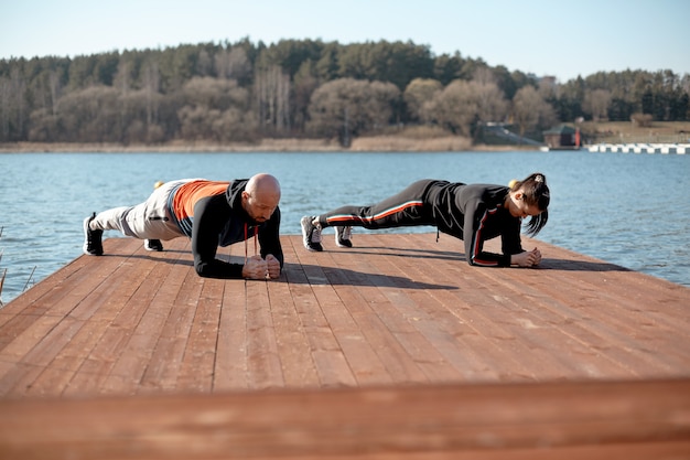 Ein Mann und ein Mädchen in Sportkleidung machen auf dem Pier am See Plankenübungen. Sport, Gesundheit, aktive Hobbys