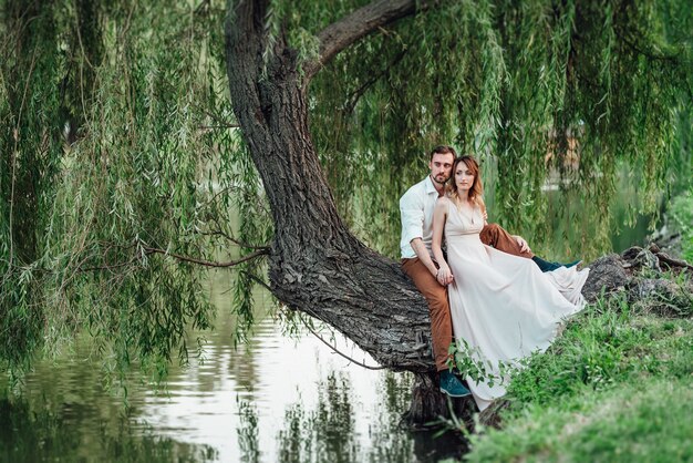 Ein Mann und ein Mädchen sitzen zusammen auf einem schiefen Baum am steilen Ufer eines wilden Flusses