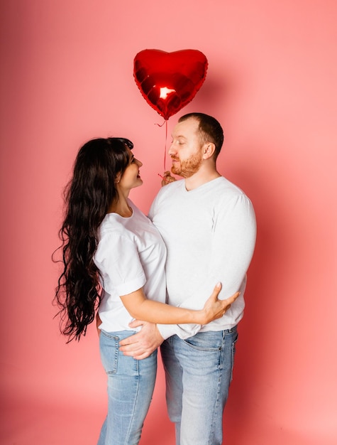 Ein Mann und eine Frau auf einem rosa Hintergrund halten einen großen aufblasbaren roten herzförmigen Ballon in ihren Händen. Feiertagskonzept - Valentinstag