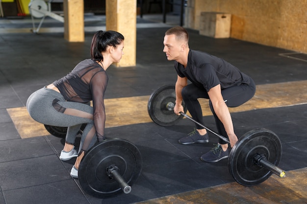 Ein Mann und eine Frau im Fitnessstudio schauen sich an, bevor sie eine Langhantel reißen