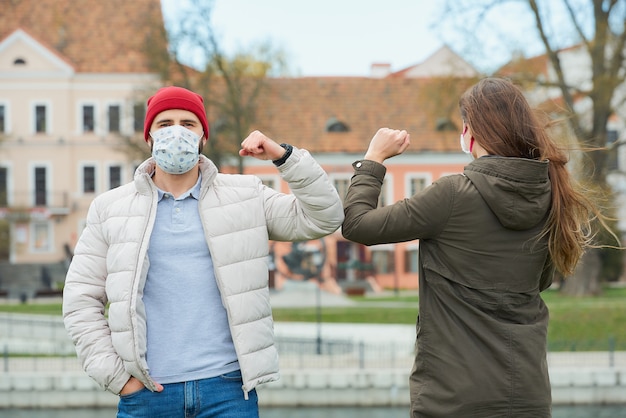 Ein Mann und eine Frau in Gesichtsmasken stoßen an die Ellbogen, anstatt sie mit einer Umarmung zu begrüßen