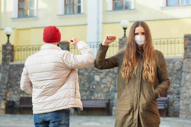 Ein Mann und eine Frau in Gesichtsmasken stoßen an die Ellbogen, anstatt sie mit einer Umarmung zu begrüßen