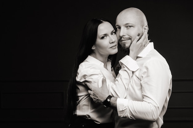 Ein Mann und eine Frau in weißen Hemden auf schwarzem Hintergrund. Ein verliebtes Paar im Studio-Interieur. Schwarz-Weiß-Foto