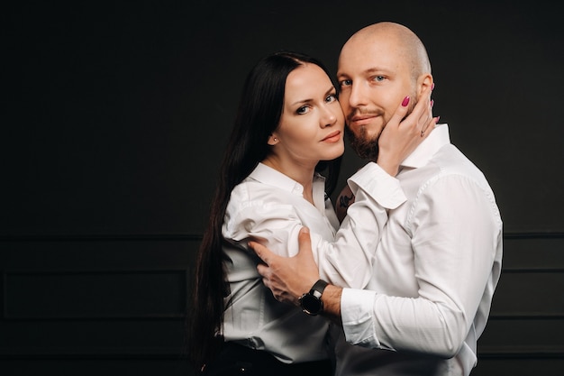 Ein Mann und eine Frau in weißen Hemden auf schwarzem Hintergrund. Ein verliebtes Paar im Studio-Interieur.