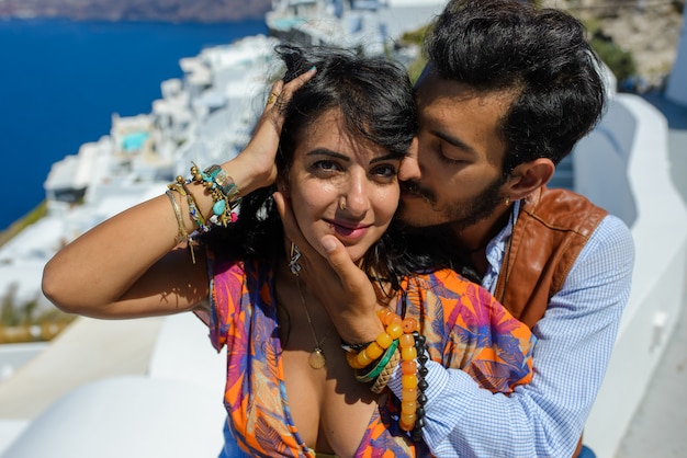 Ein Mann und eine Frau küssen sich vor dem Hintergrund des Skaros Rock auf Santorini Island. Das Dorf Imerovigli. Er ist ein ethnischer Zigeuner. Sie ist eine Israeliin.