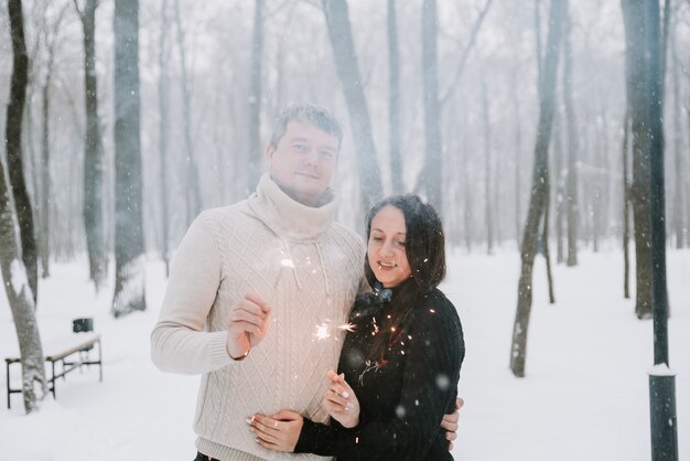 Ein Mann und eine Frau mit Wunderkerzen auf dem Hintergrund eines schneebedeckten Waldes in einem Schneefall