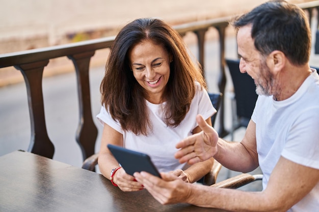 Ein Mann und eine Frau mittleren Alters benutzen das Touchpad und sitzen auf der Tischterrasse eines Cafés.