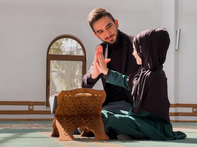 Ein Mann und eine Frau sitzen in einer Moschee auf dem Boden, beide tragen Hijab und einen schwarzen Hijab.