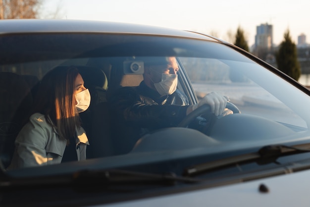 Ein Mann und eine Frau tragen medizinische Masken und Gummihandschuhe, um sich beim Autofahren vor Bakterien und Viren zu schützen. maskierte Männer im Auto. Coronavirus (COVID-19