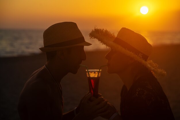 Ein Mann und eine Frau trinken einen Cocktail bei Sonnenuntergang am Meer. Selektiver Fokus.