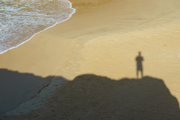 Ein Mann und sein Schatten sind am Strand und das Wasser schäumt