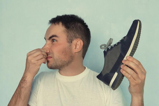 Ein Mann verschließt sich die Nasenlöcher wegen des Geruchs, der von dem Sportschuh ausgeht, den er in der Hand hält