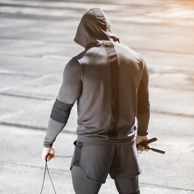 Ein Mann von sportlicher Statur auf einem Sportplatz in einem grauen Sportanzug Der Mann steht mit dem Rücken