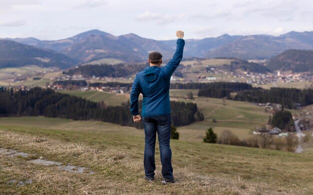 Ein Mann vor dem Hintergrund einer wunderschönen Alpenlandschaft winkt mit der Hand