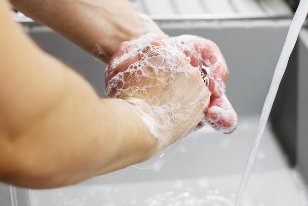 Ein Mann wäscht seine Hände mit Seife unter fließendem Wasser aus nächster Nähe. Gesundheits-, Sauberkeits- und Hygienekonzept.