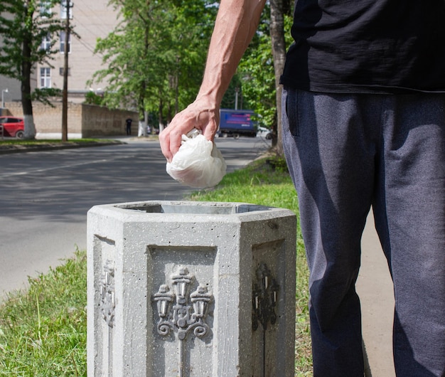 Ein Mann wirft eine Plastiktüte in den Mülleimer. Müllverwertung auf der Straße. Straßenurne