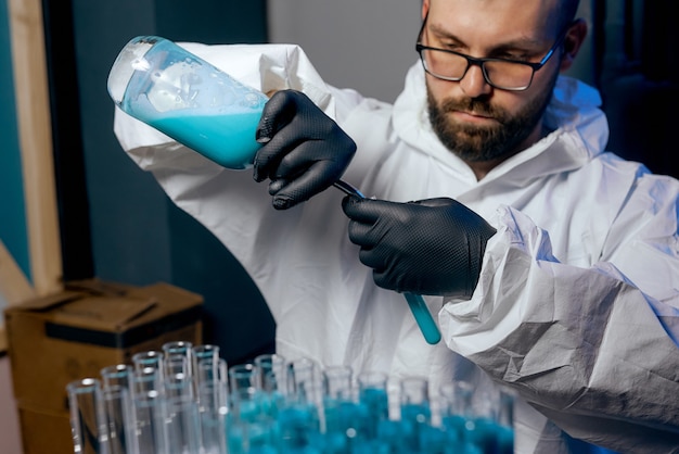 Ein Mann Wissenschaftler in einem Schutzanzug mit Flaschen in den Händen mit einem blauen Impfstoff