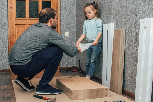 Ein Mann zu Hause sammelt Möbel mit seinen eigenen Händen, seine kleine Tochter hilft ihm