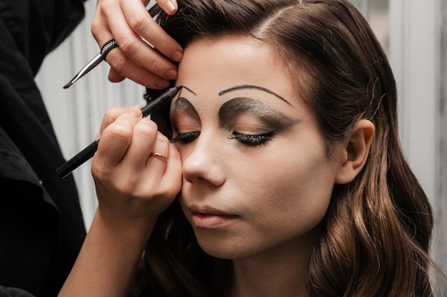 Ein Maskenbildner macht Kunst-Make-up für ein junges Mädchen in einem Schönheitssalon. Das Konzept, Halloween zu feiern. Ungewöhnliches Make-up